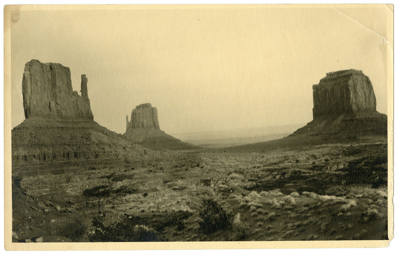 Sepia-toned archival photograph of Monument Valley's sandstone buttes rising from a desert landscape under a hazy sky