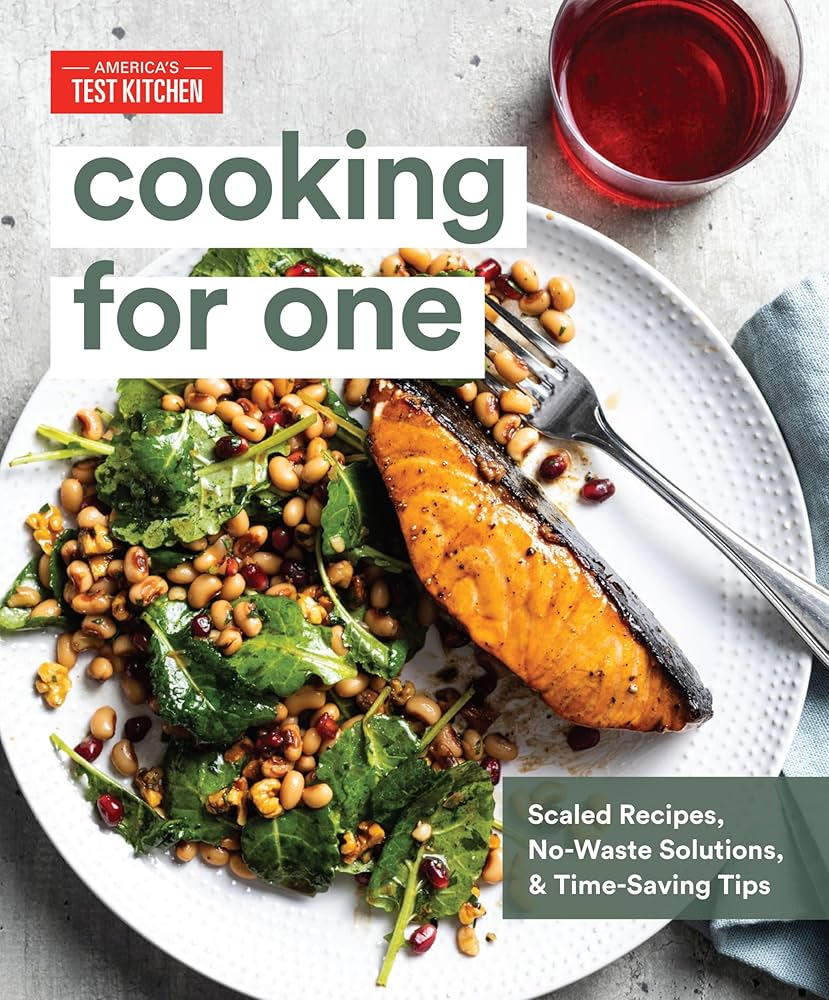 Book cover for Cooking for One by America's Test Kitchen. A plated meal of seared salmon, black-eyed peas, greens, and pomegranate seeds sits on a textured white plate beside a glass of red wine.
