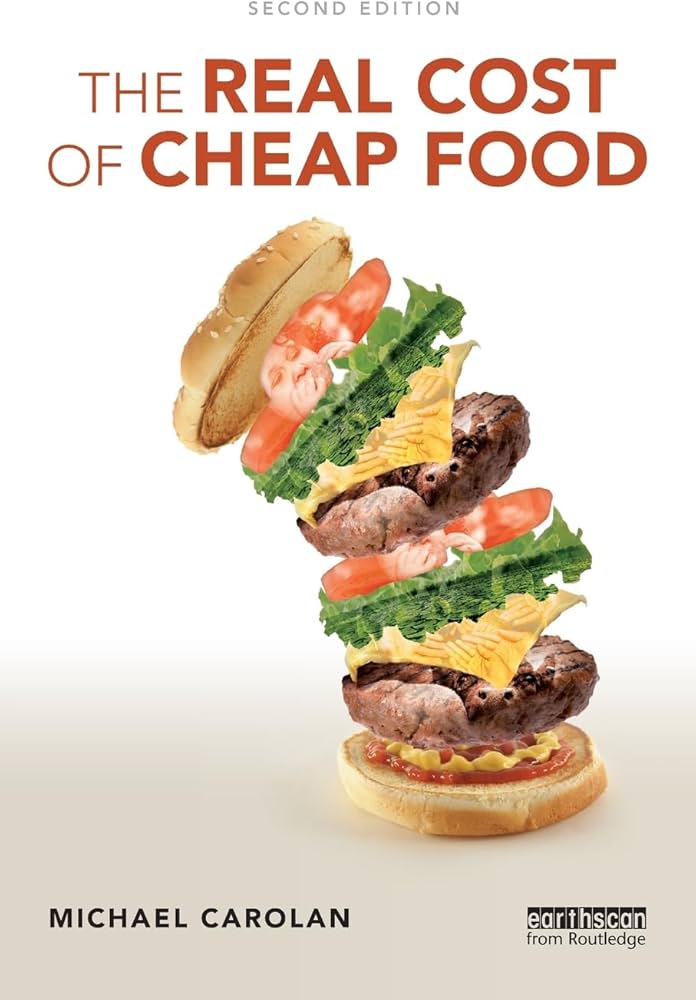 Book cover for The Real Cost of Cheap Food by Michael Carolan. A hamburger appears mid-air, its layers separating and falling apart against a plain white background.