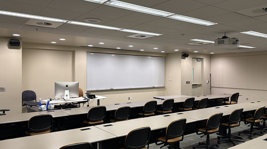 Classroom 155 - Two rows of tables and chairs. Front wall has a whiteboard and is projector capable.