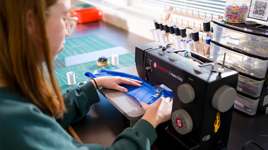 A person sews blue fabric with a sewing machine in a workspace.