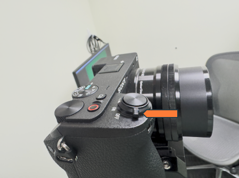 A close-up of a Sony mirrorless camera showing the top controls, with an orange arrow pointing to the On/Off switch beside the shutter button.