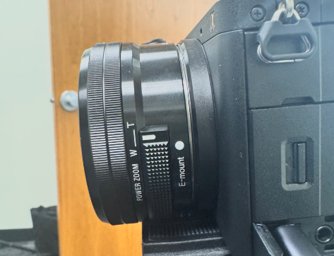 A close-up side view of a Sony E-mount power-zoom lens, highlighting the W–T zoom rocker and textured zoom ring.
